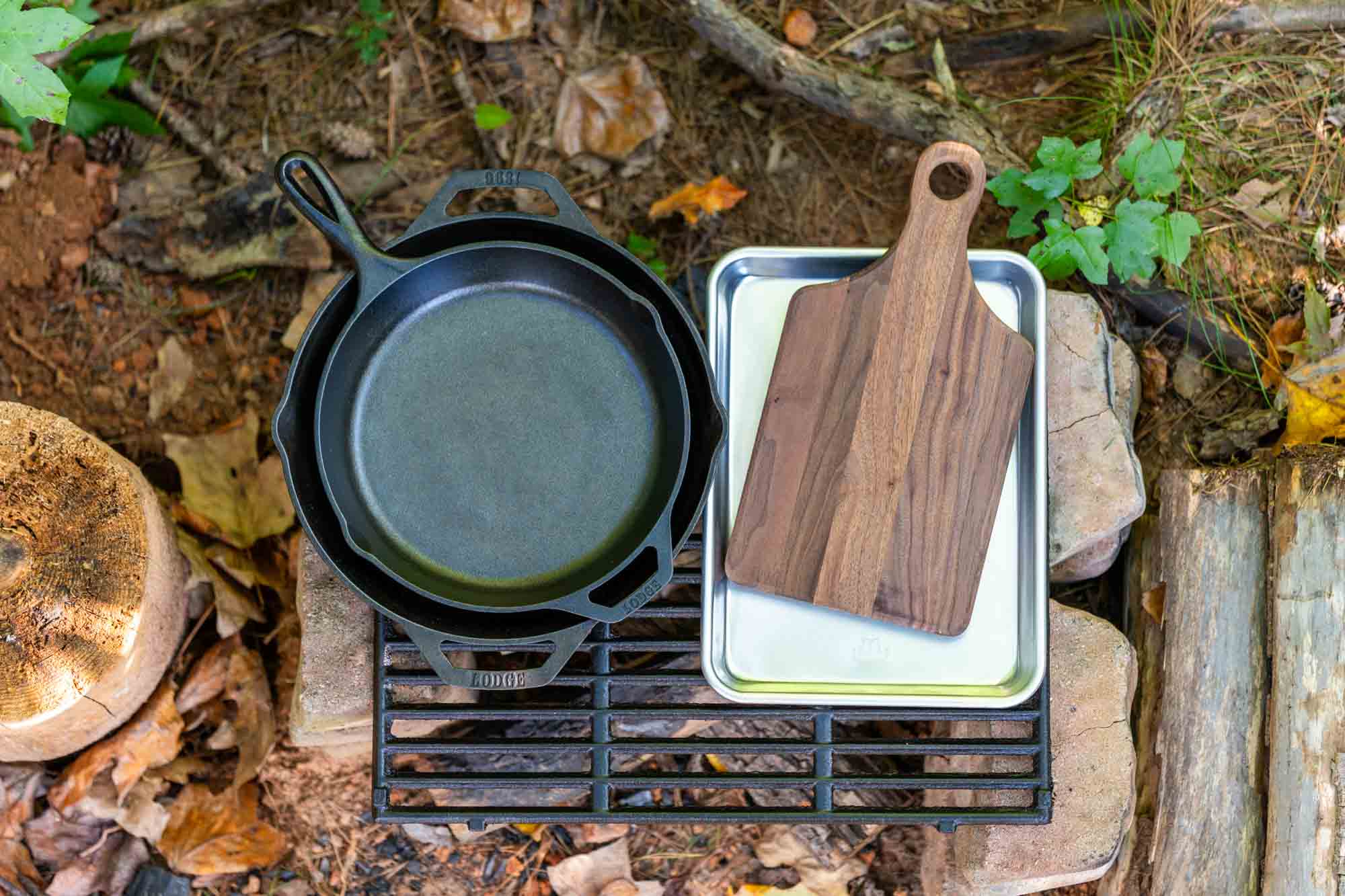 Lodge cast iron skillet, Made In sheet pan, and Etched Timber cutting board on a camp grill grate